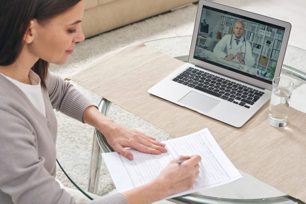A woman is sitting at a table with a laptop in front of her, contemplating group health insurance options.