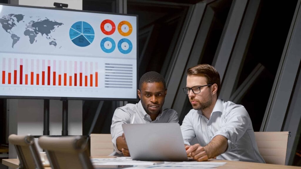 Two professionals analyzing data on laptop and screen.