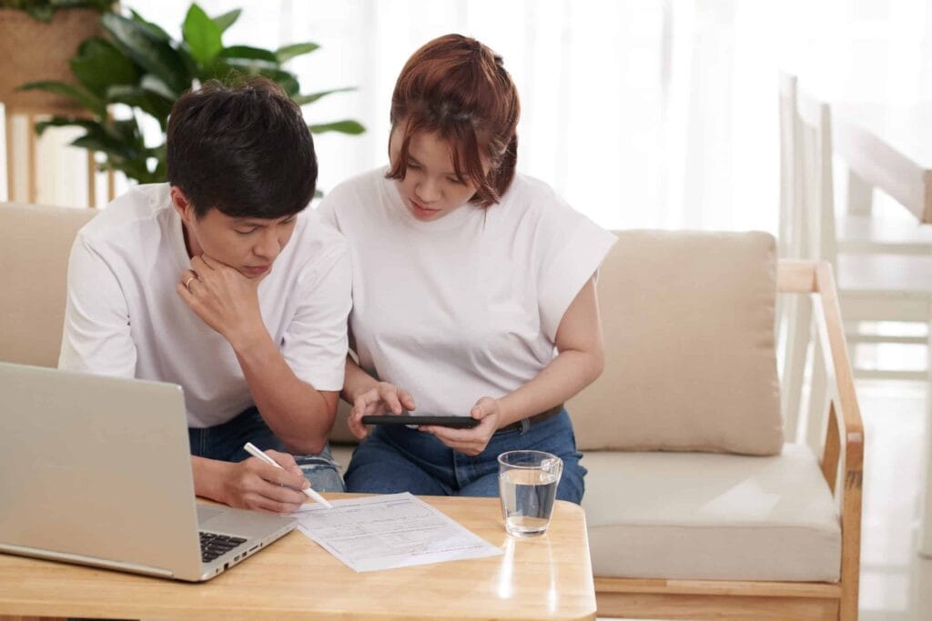 A man and woman sitting on a couch, discussing why health care reform has failed while looking at a laptop.