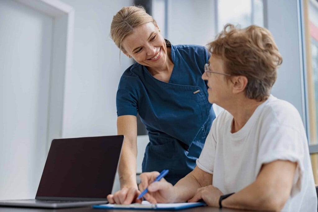 A nurse is assisting an elderly woman with a laptop for health insurance.