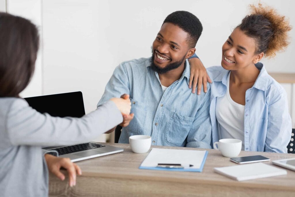 A couple shaking hands with a real estate agent, showcasing skilled negotiation.