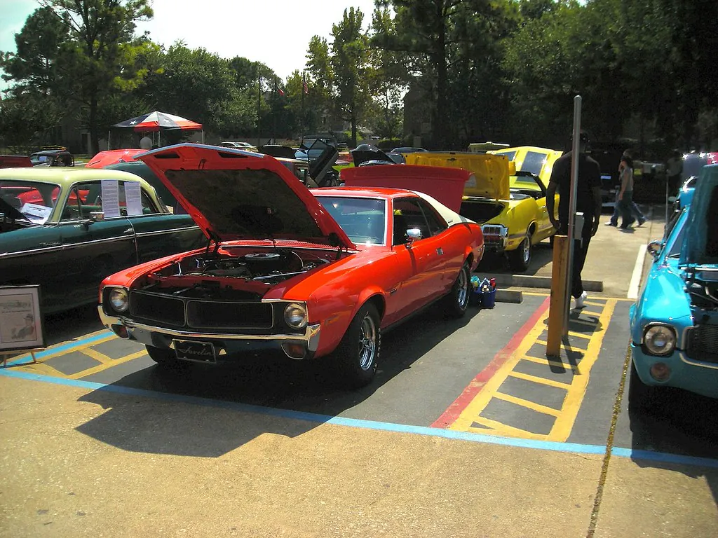 Classic car show in Greater Greenspoint featuring a red vintage car with its hood open, surrounded by other classic vehicles in a parking lot.