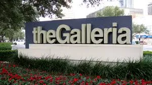 Sign reading 'The Galleria' surrounded by greenery and red flowers in Galleria, TX, representing the location for custom health plans and affordable group coverage.