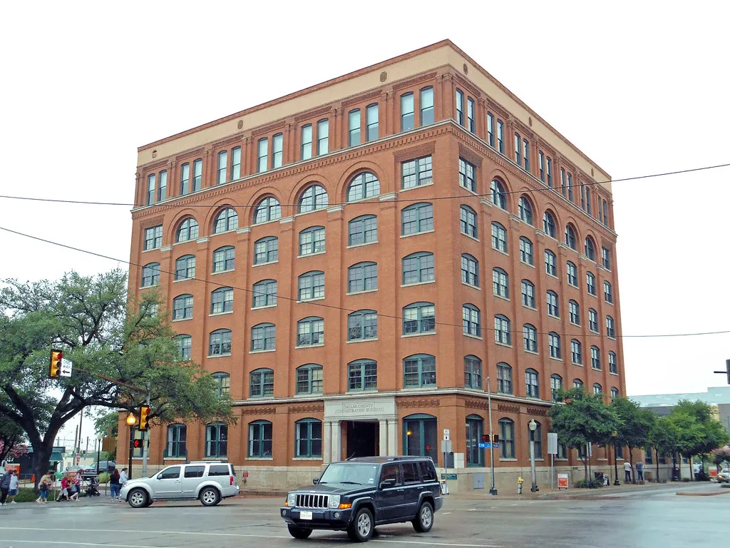 Historic red brick building with multiple windows, located at a street corner with several cars and pedestrians, representing potential office locations for Pearland Group Health Insurance solutions.