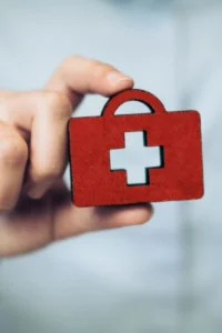 Hand holding a red first aid kit icon with a white medical cross symbol.